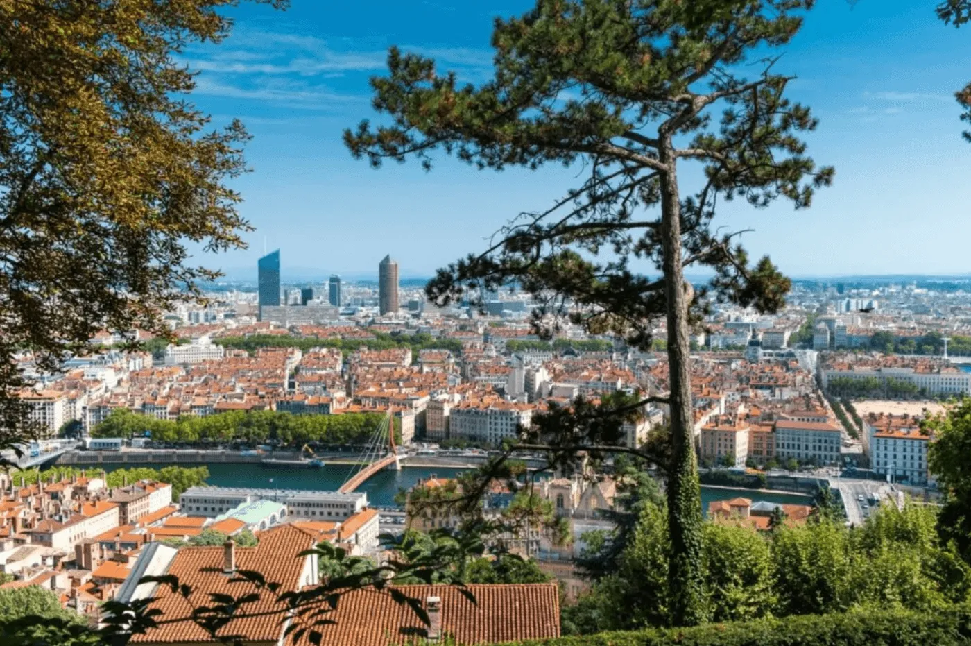 Vue panoramique de Lyon depuis la colline de Fourvière montrant la Saône, la Passerelle Saint-Georges et les gratte-ciel de la Part-Dieu (Incity et Tour Part-Dieu) sous un ciel bleu.